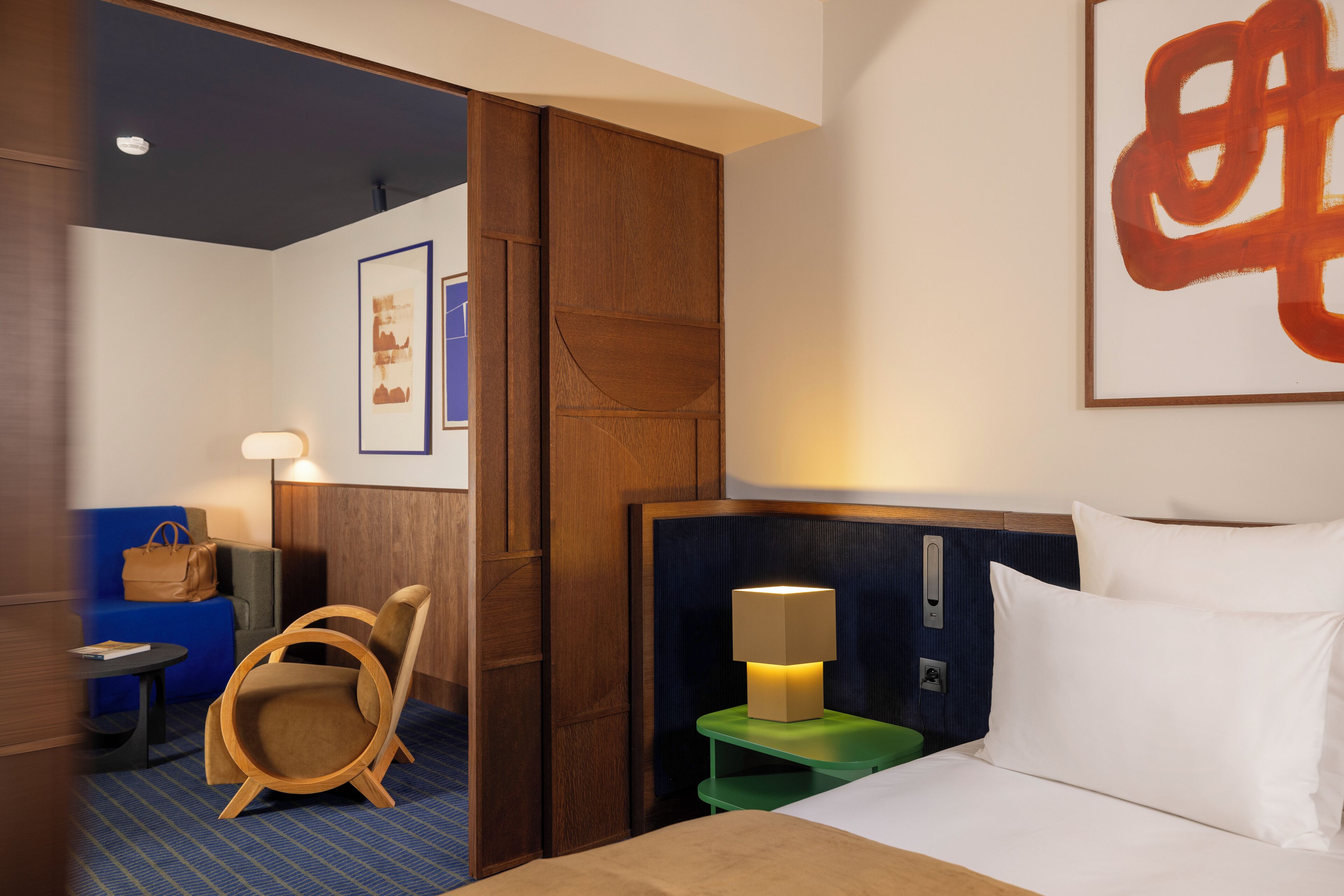 Habitación de hotel con cama, mesita de noche con lámpara, una silla, sofá azul y armario de madera.