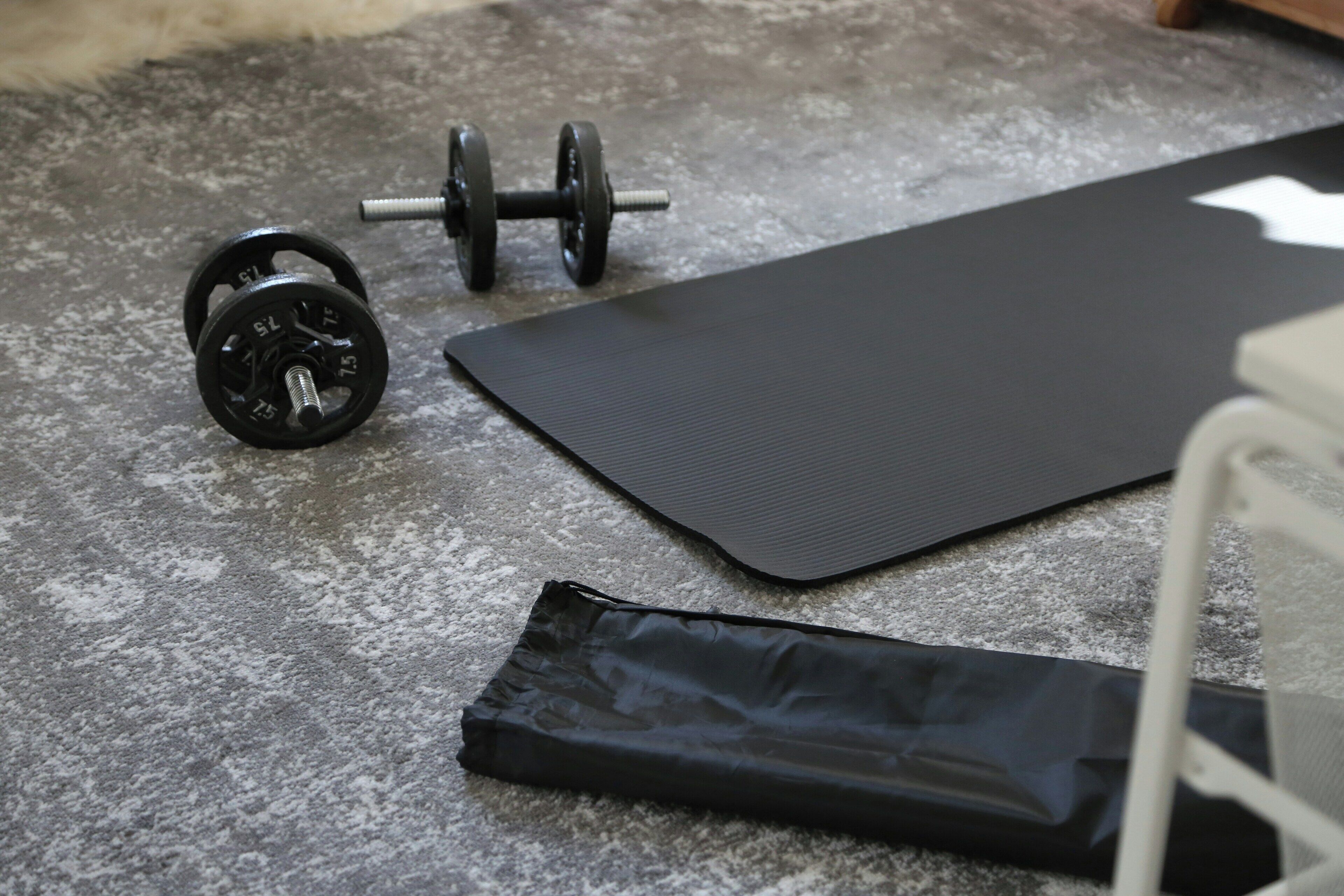 A gym with a black exercise mat, a barbell, and weight plates on a concrete floor.