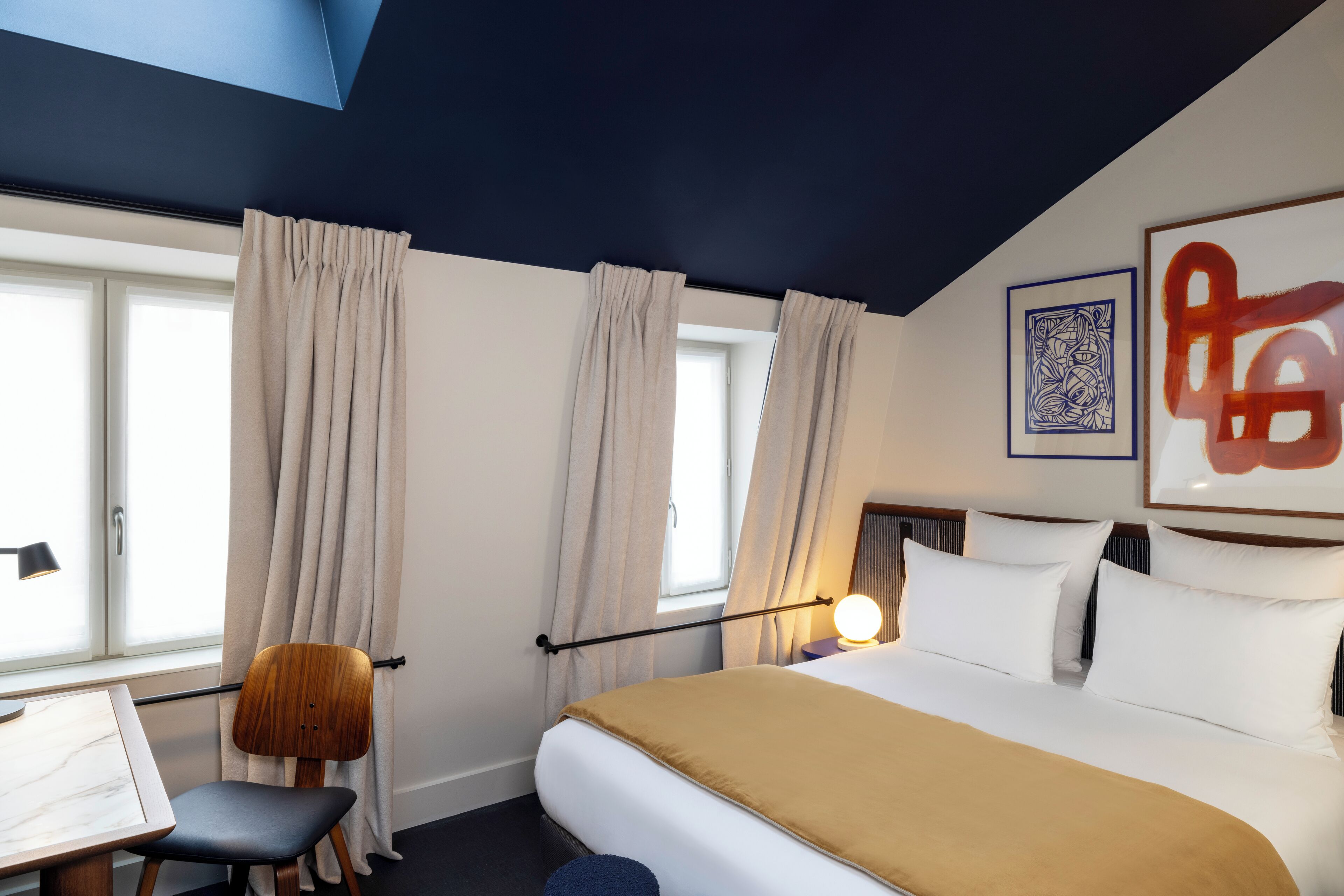 A hotel room with a bed, a desk, a chair, and a window with curtains.