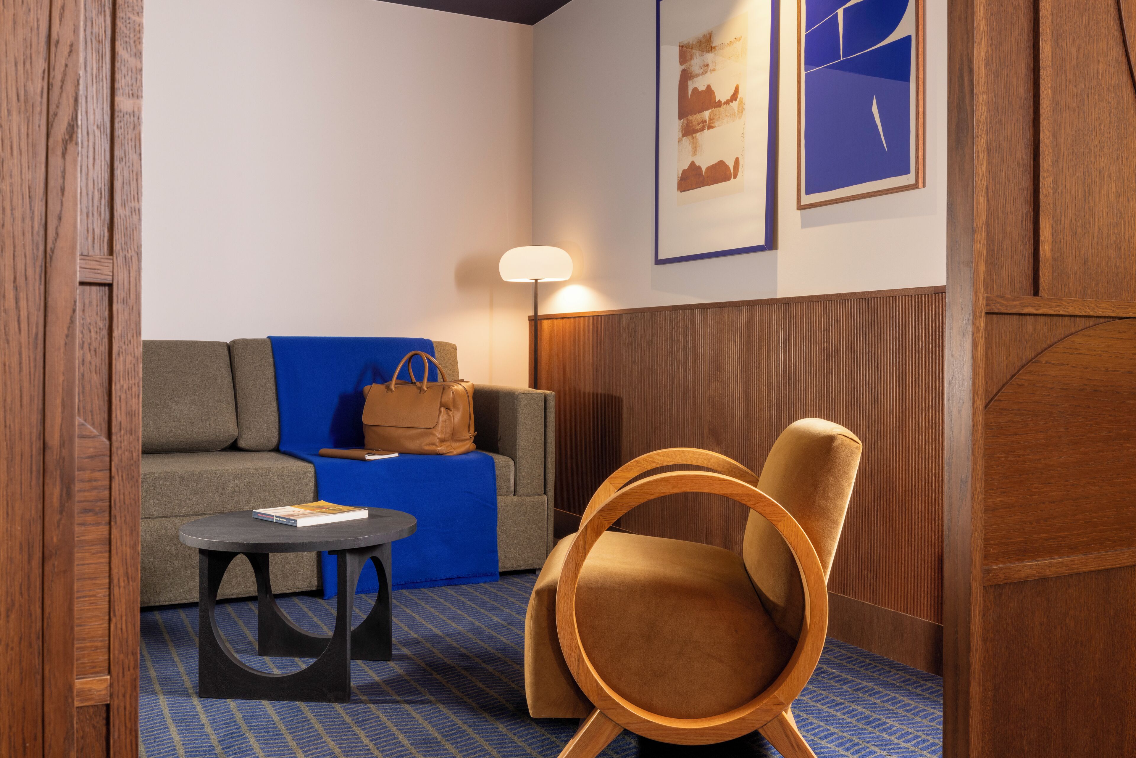 Une chambre d’hôtel moderne avec un canapé, une chaise en bois, une petite table et une lampe.