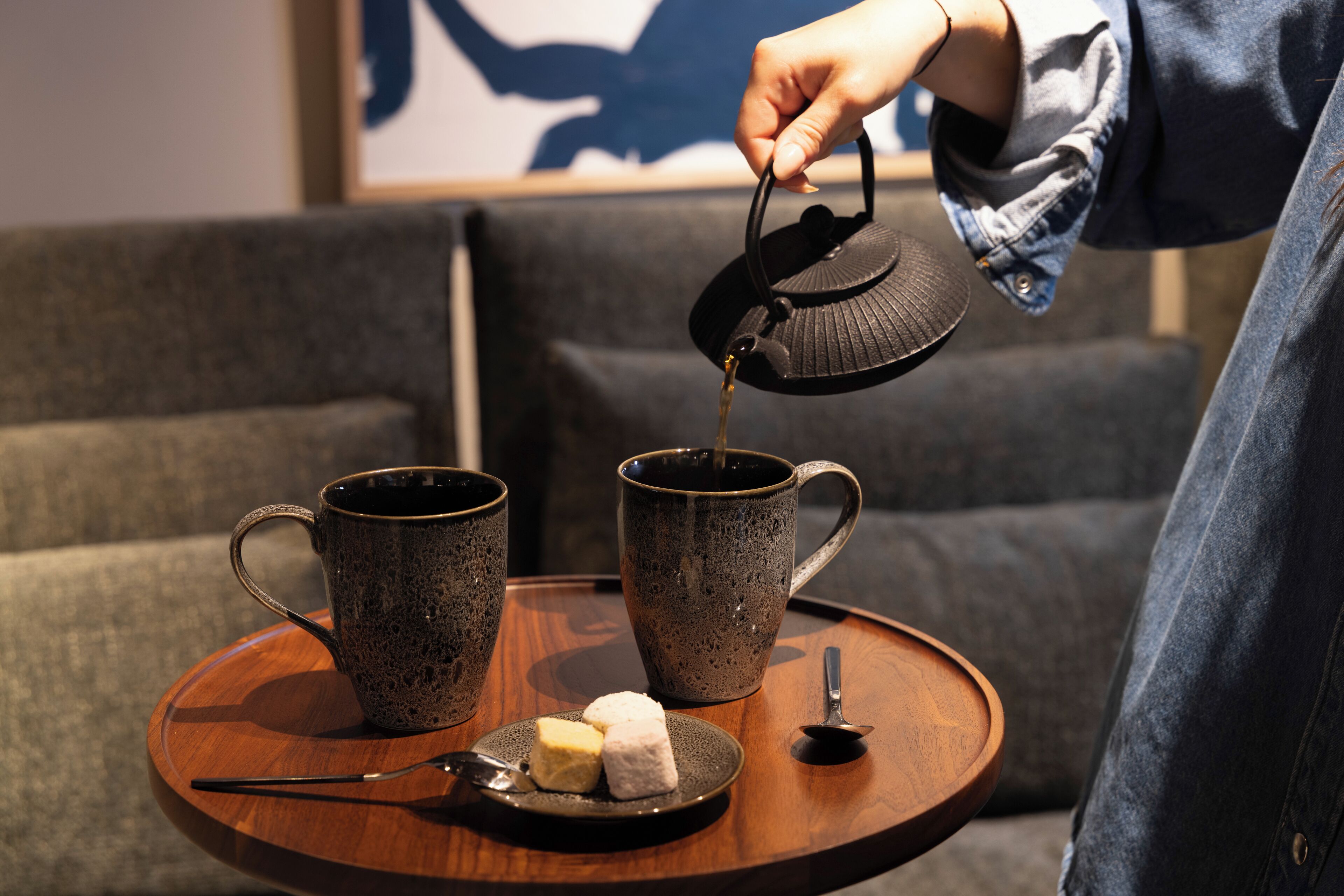 Eine Person gießt Tee in eine Tasse auf einem Tablett, zusammen mit zwei weiteren Tassen und einem Teller mit zwei Zuckerwürfeln.