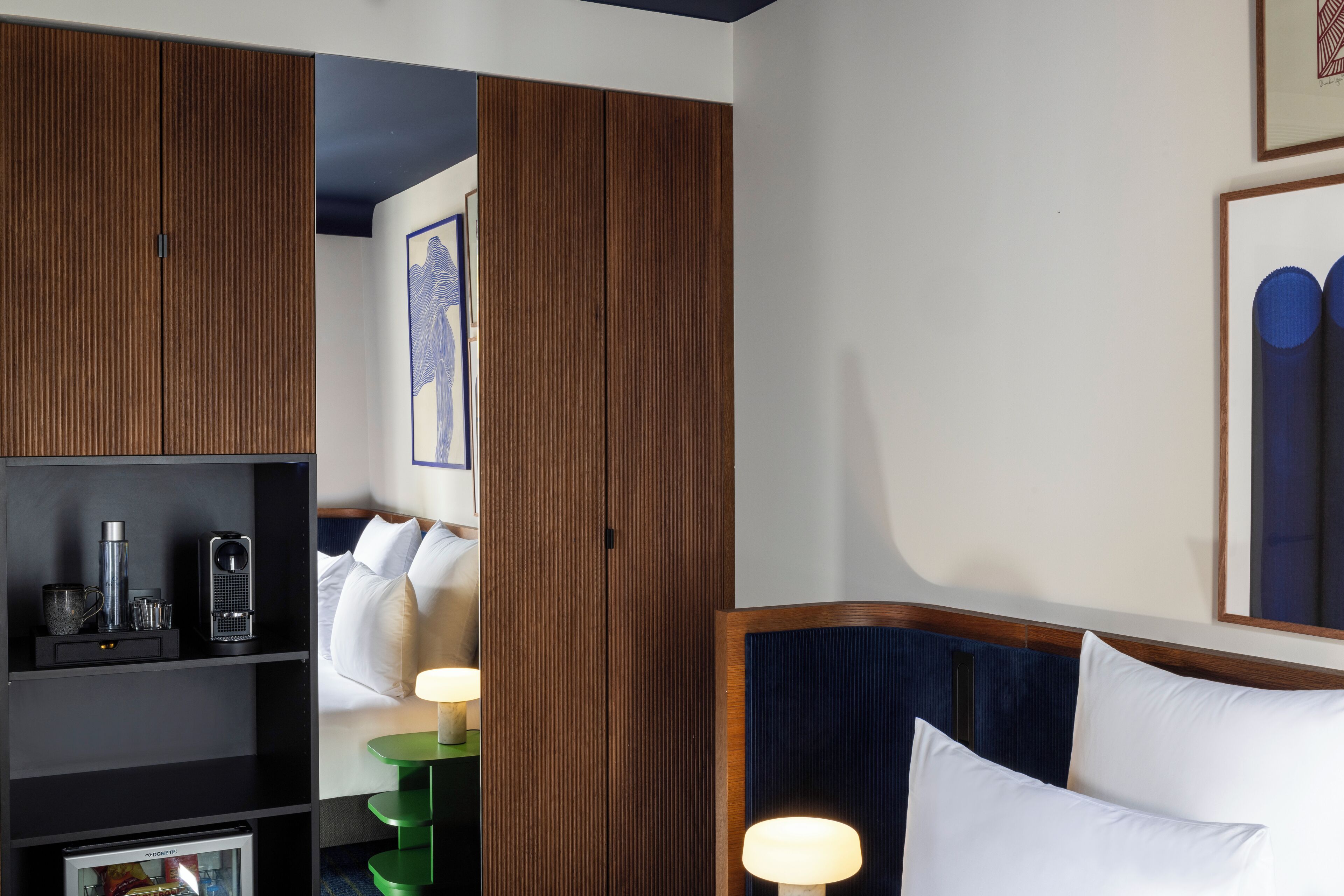 Una habitación de hotel con una cama, una mesita de noche, un estante con objetos y un armario de madera.