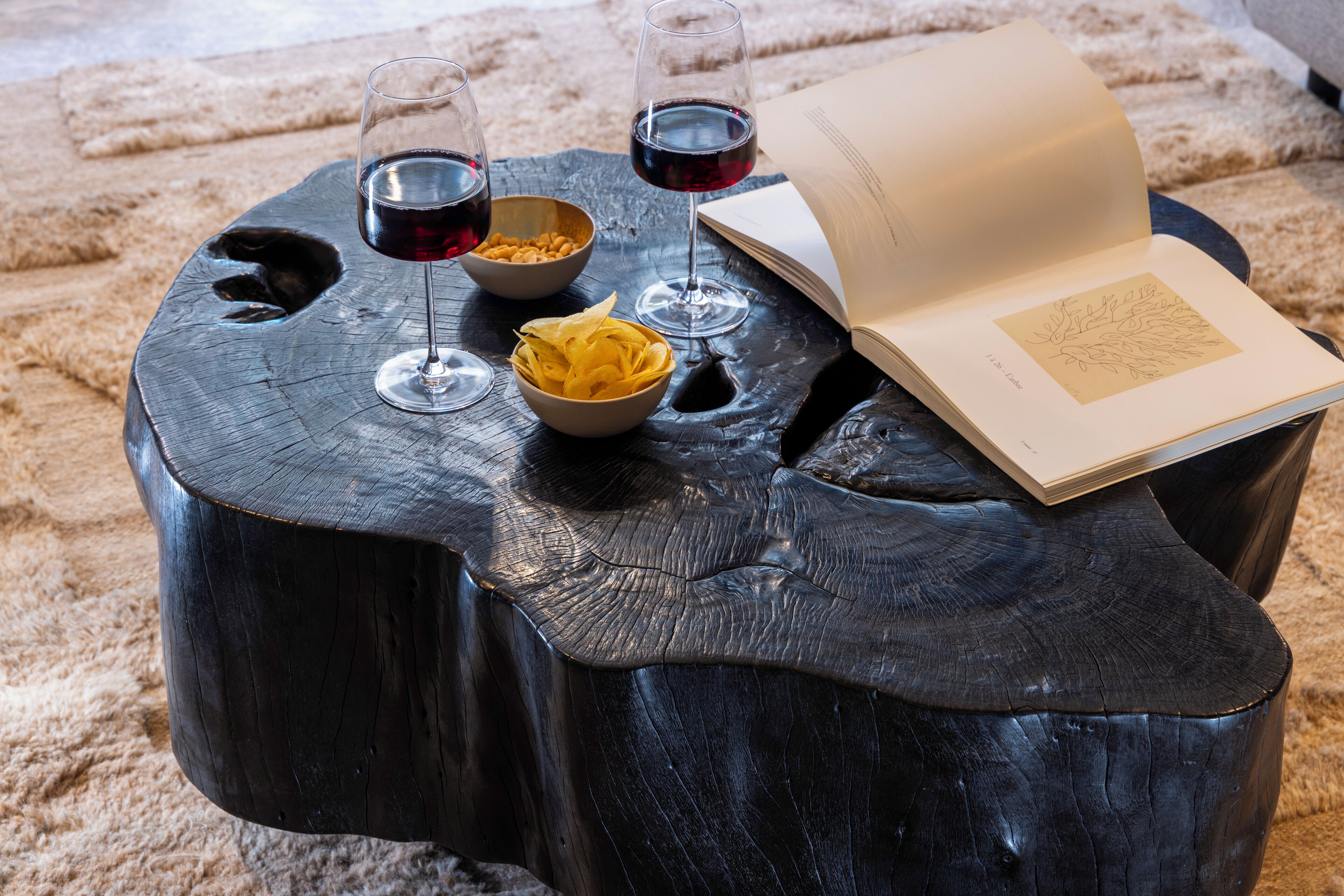 Een ronde houten tafel met twee wijnglazen en een schaal lekkernijen, vergezeld van een open boek.