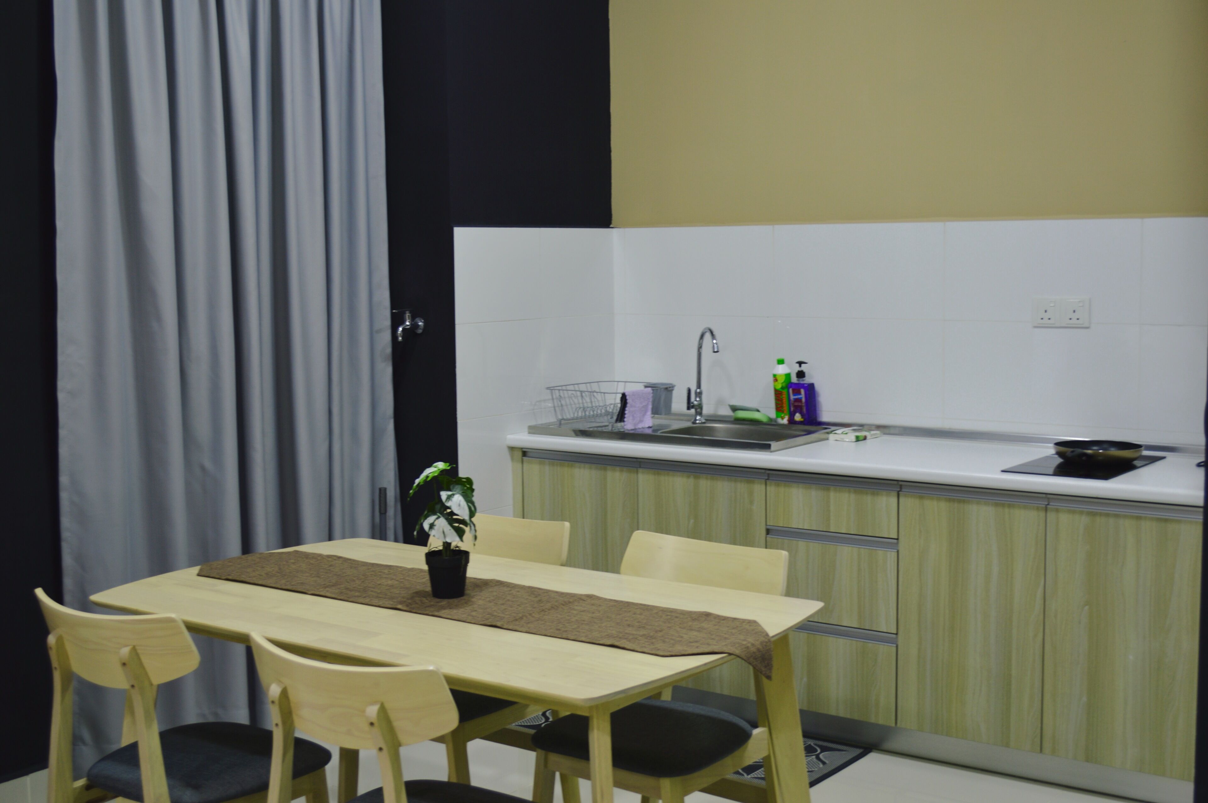 A compact kitchen with a dining area, including a table with chairs, a sink, and a small countertop with a plant and cleaning supplies.