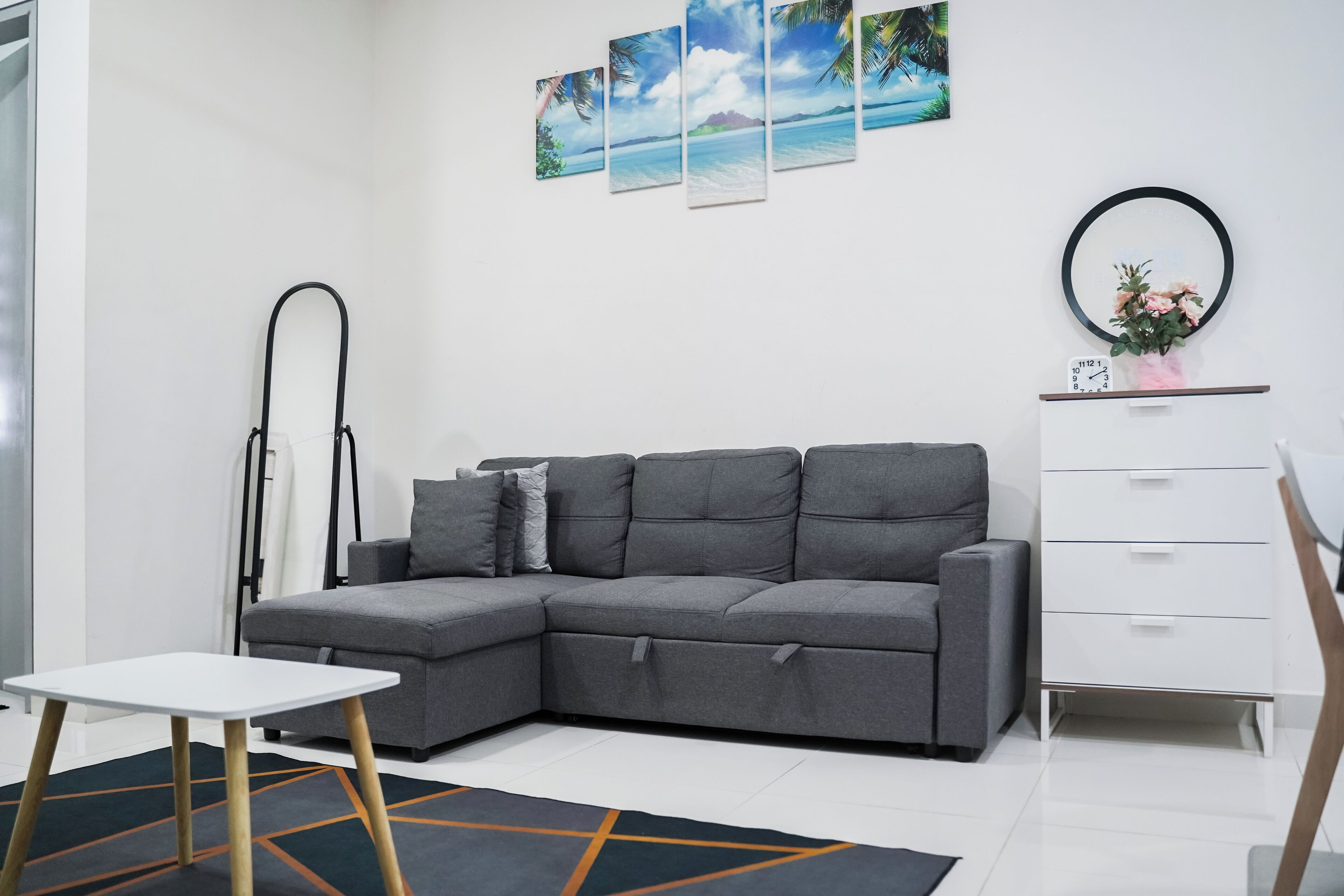 Una sala de estar moderna con un sofá seccional gris, una mesita auxiliar blanca, una lámpara de pie negra y un aparador blanco con cajones.