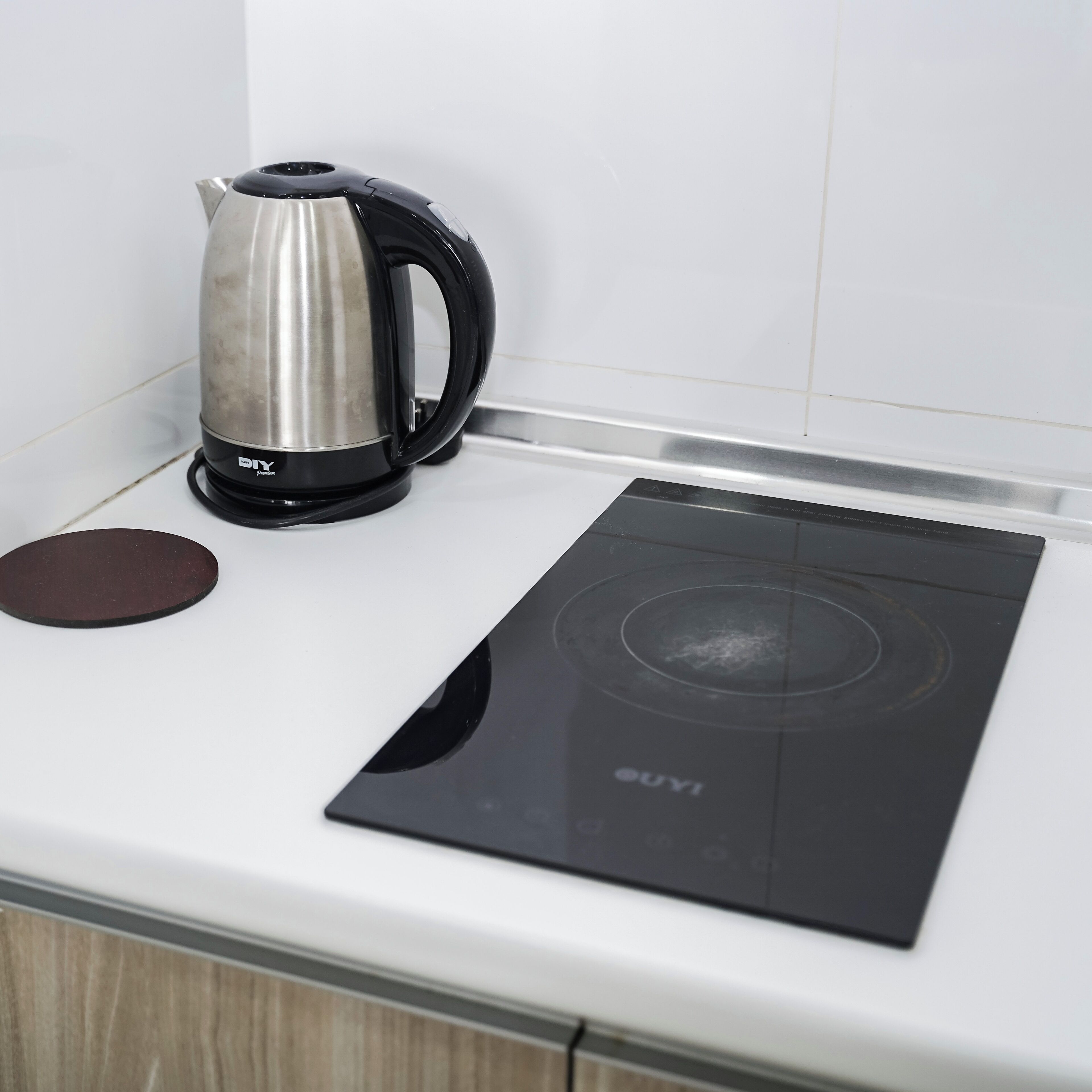 A kitchen with a black induction cooktop and a stainless steel kettle on a white countertop.