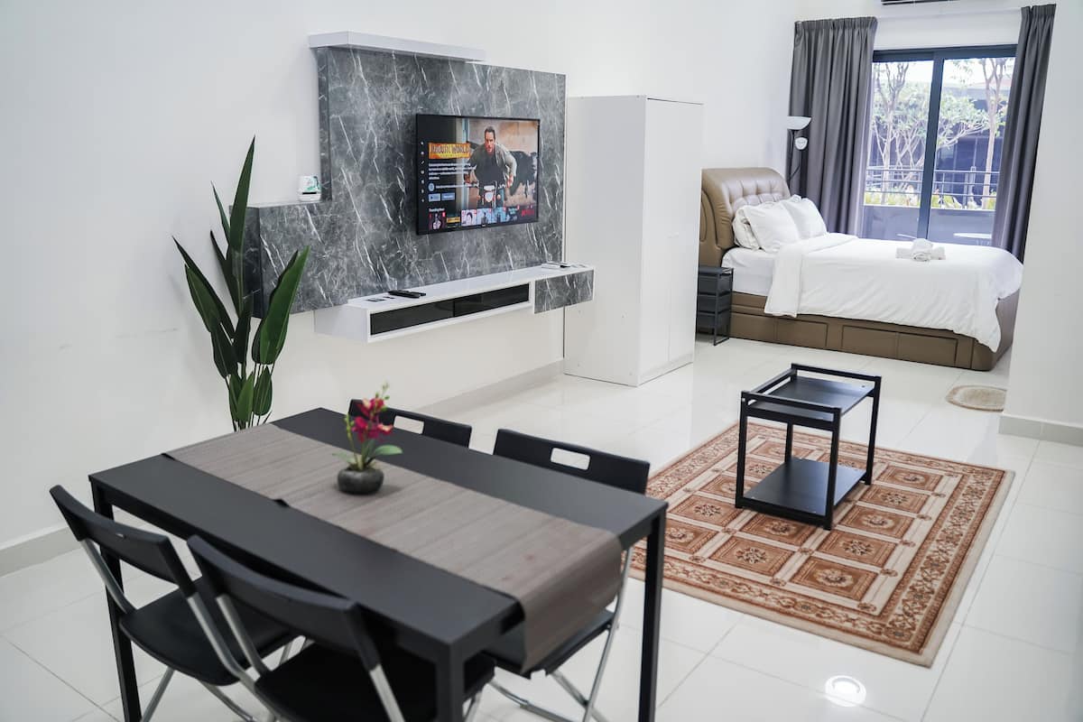 A modern hotel room with a TV mounted on a marble wall, a bed with a view to the outside, a dining area with a table and chairs, and a small side table.