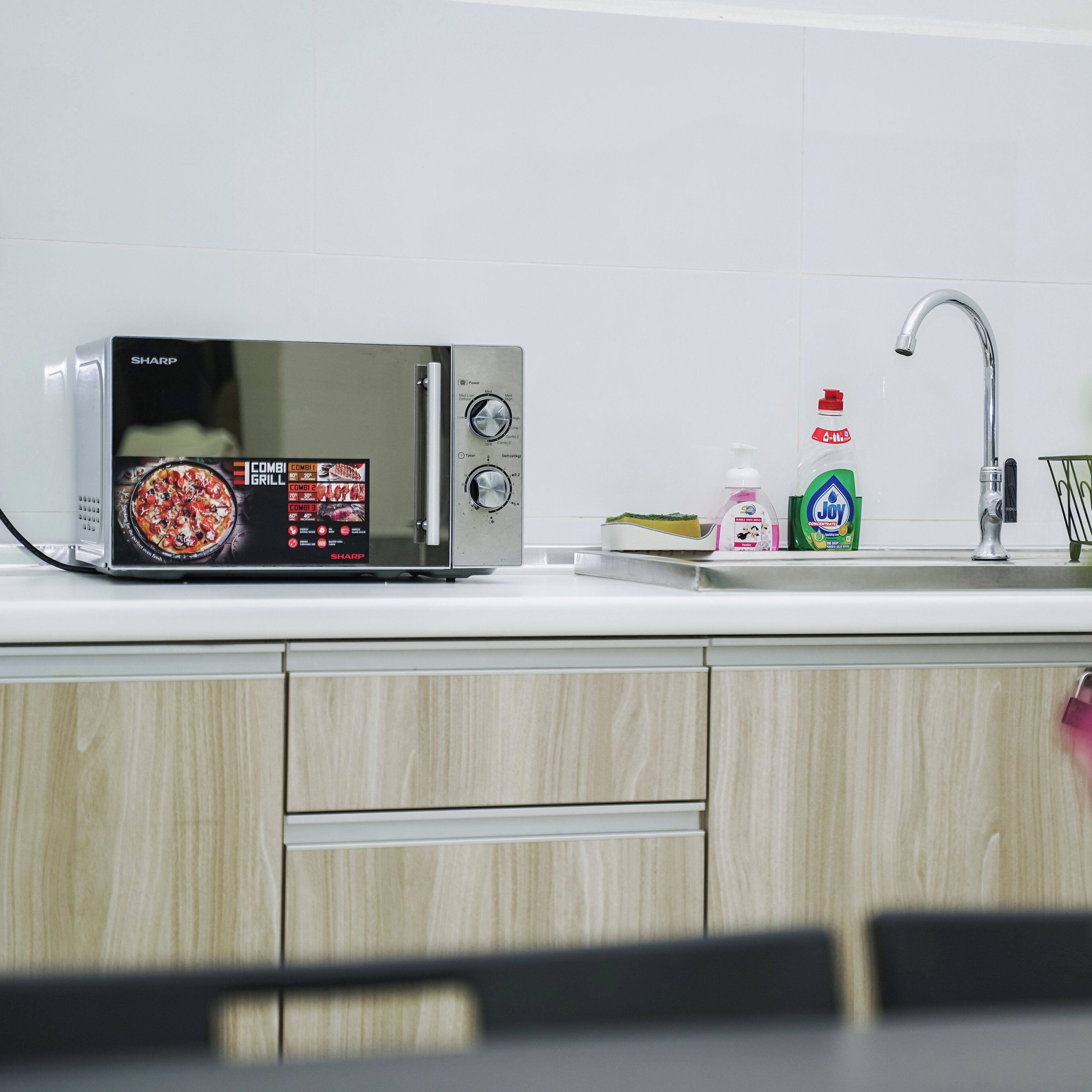 Una cucina con un forno a microonde, un lavandino e prodotti per la pulizia.