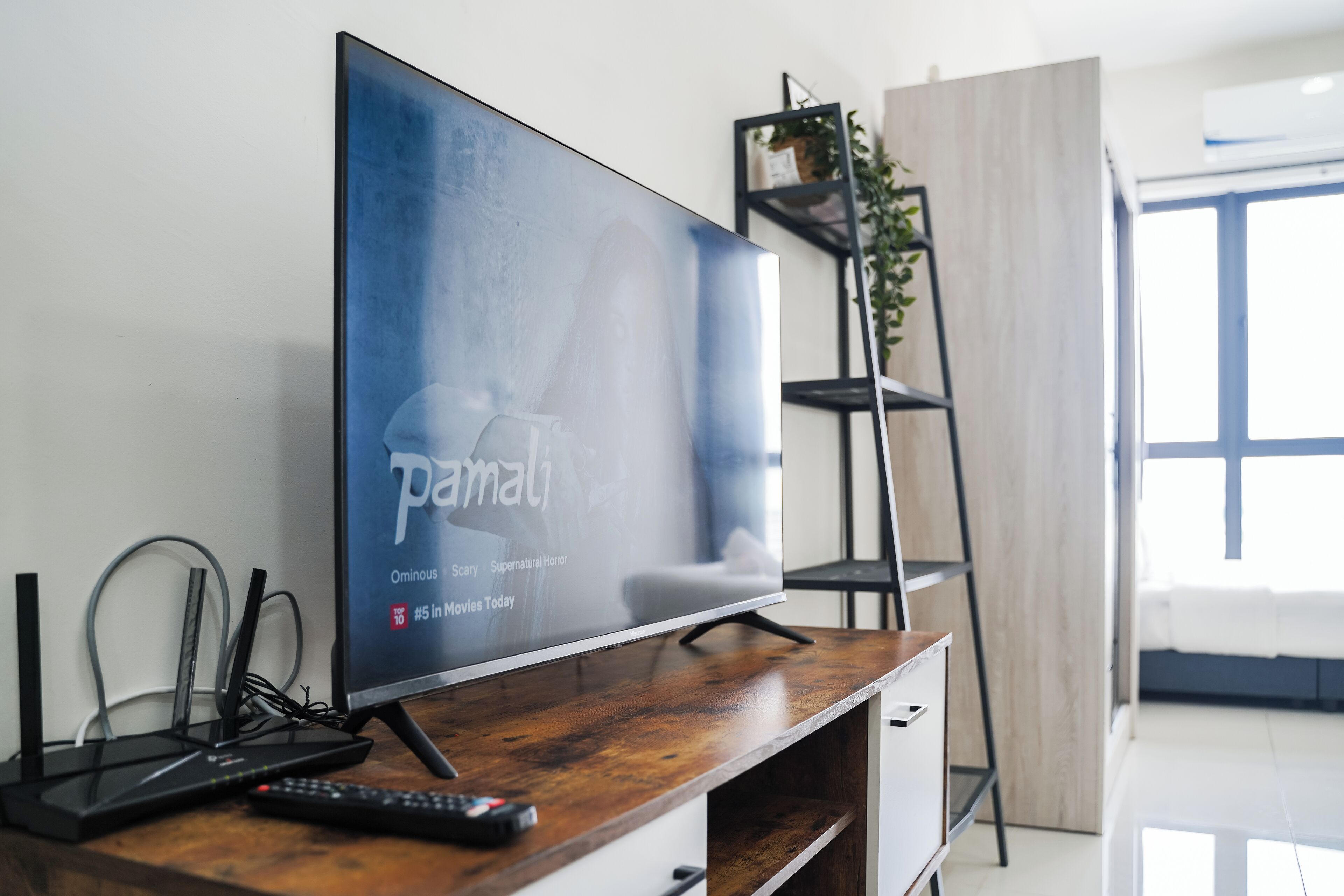 Uma sala de estar moderna com uma televisão de tela plana em um suporte de madeira, um controle remoto e uma prateleira preta com uma planta.