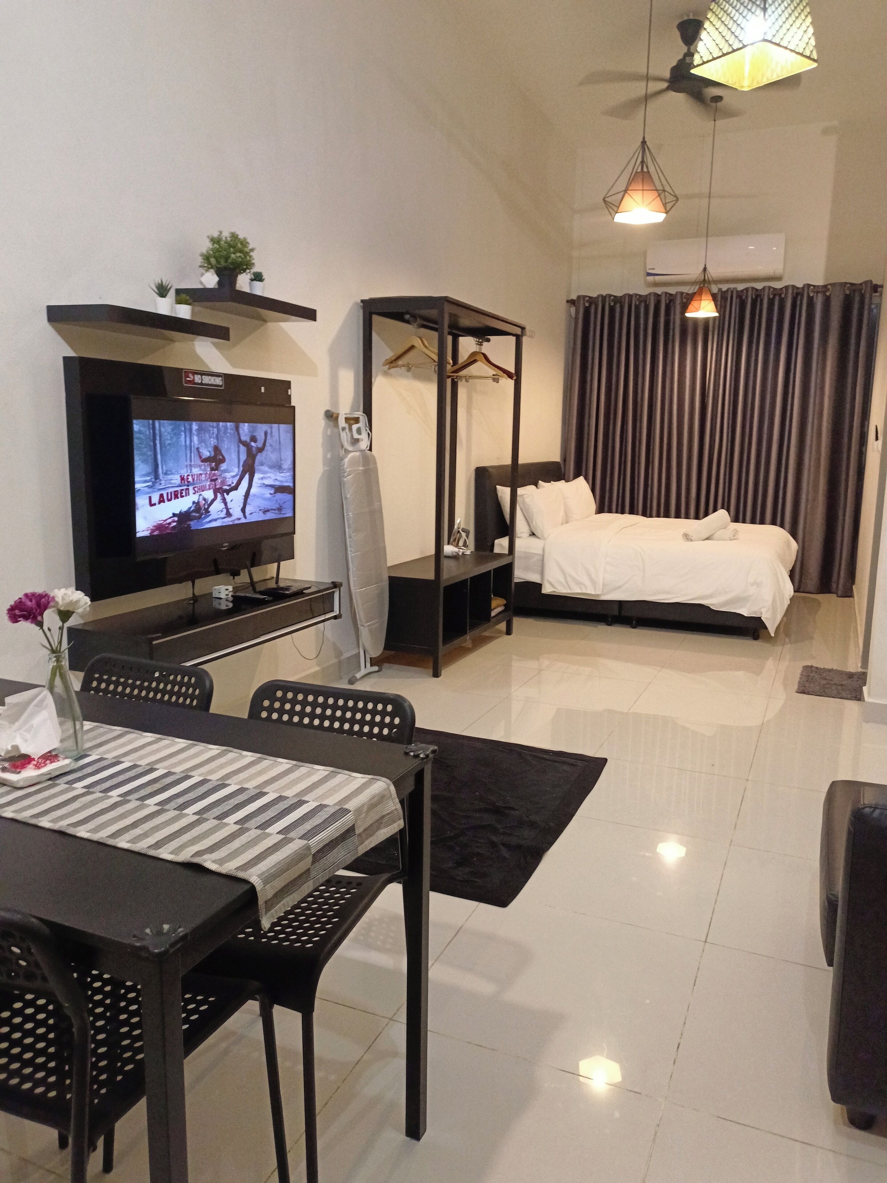 A modern hotel room with a TV, a bed, a dining area, and a ceiling fan.