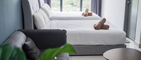Une chambre d’hôtel moderne, dotée d’un canapé, de deux lits et offrant une vue sur la verdure grâce à de grandes fenêtres.