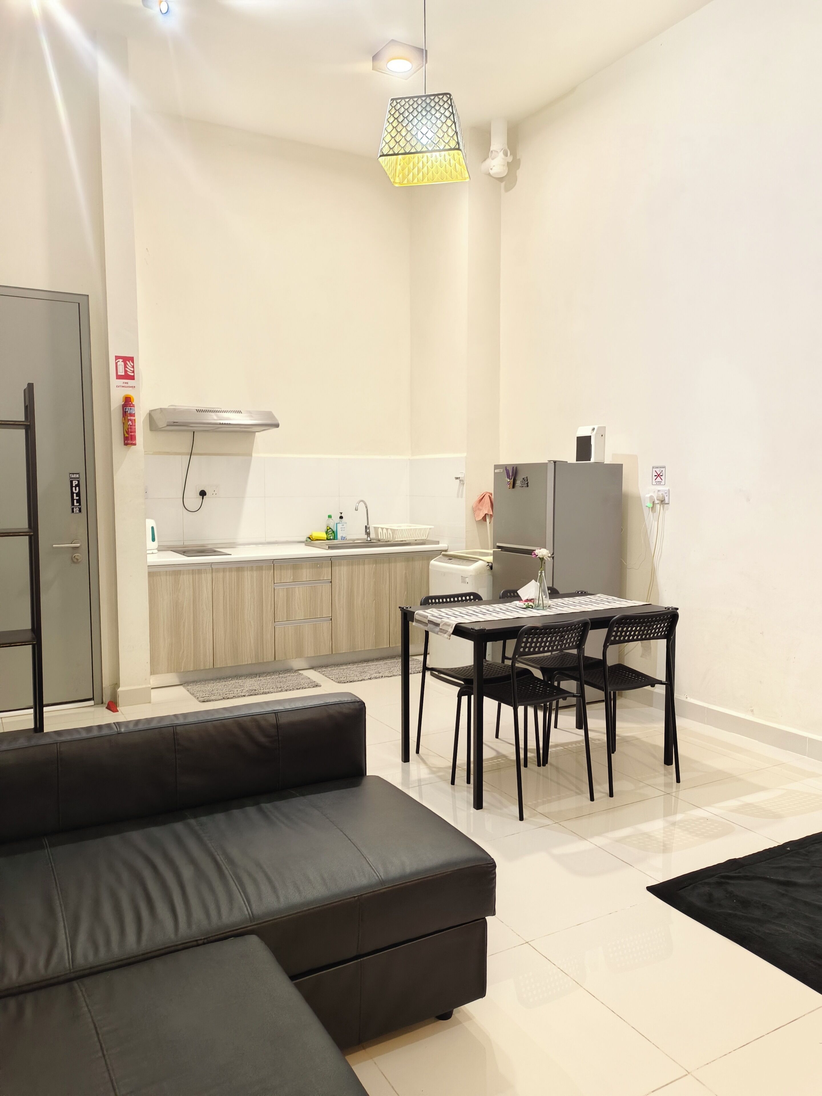 A modern living room with a black sofa, a dining table with four chairs, and a kitchen area in the background.