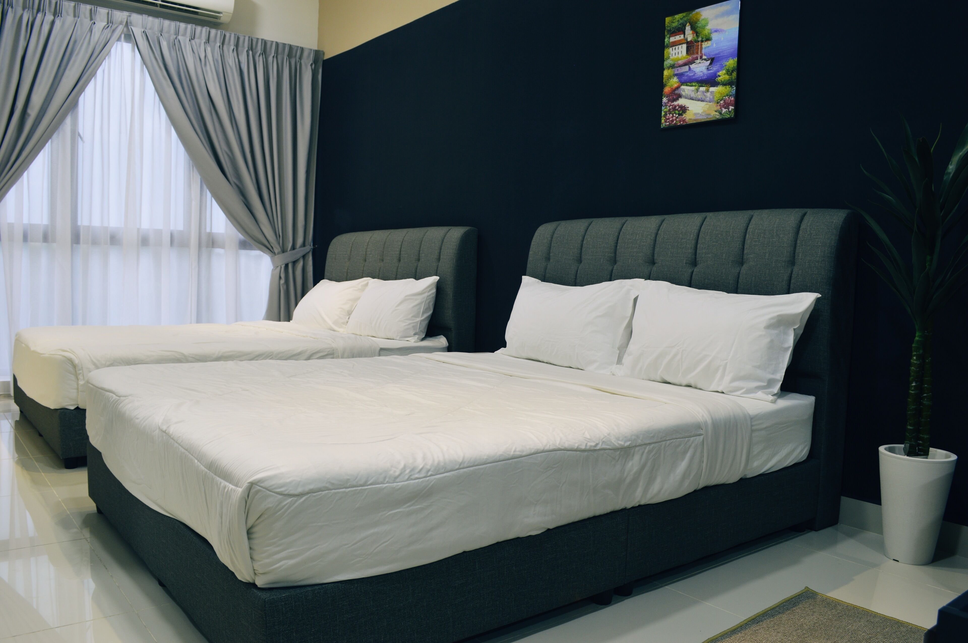 Una habitación de hotel moderna con dos camas, un ventanal con cortinas, una planta en maceta y un cuadro en la pared.