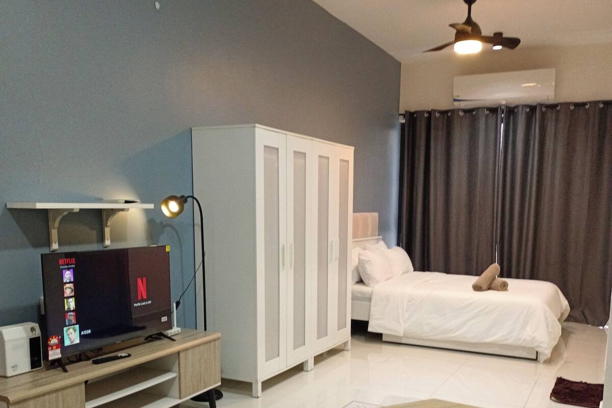 A modern hotel room with a TV, wardrobe, bed, and a ceiling fan.