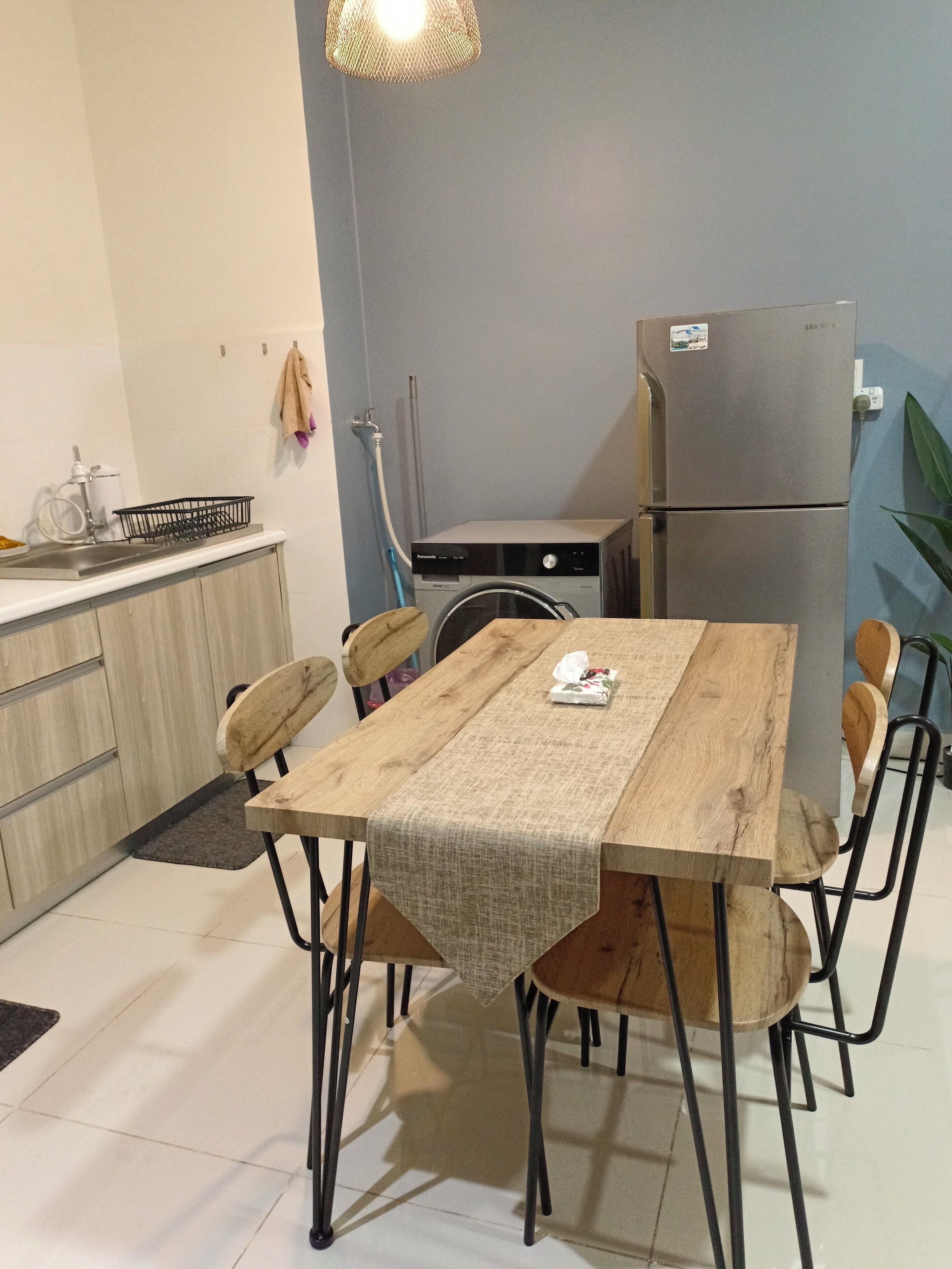 A compact kitchen with a wooden table, chairs, a refrigerator, and a washing machine.