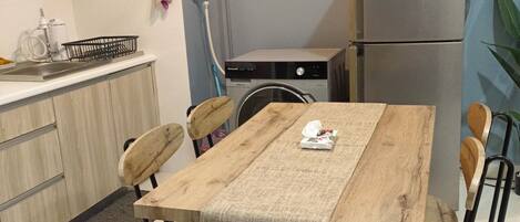A compact kitchen with a wooden table, chairs, a refrigerator, and a washing machine.