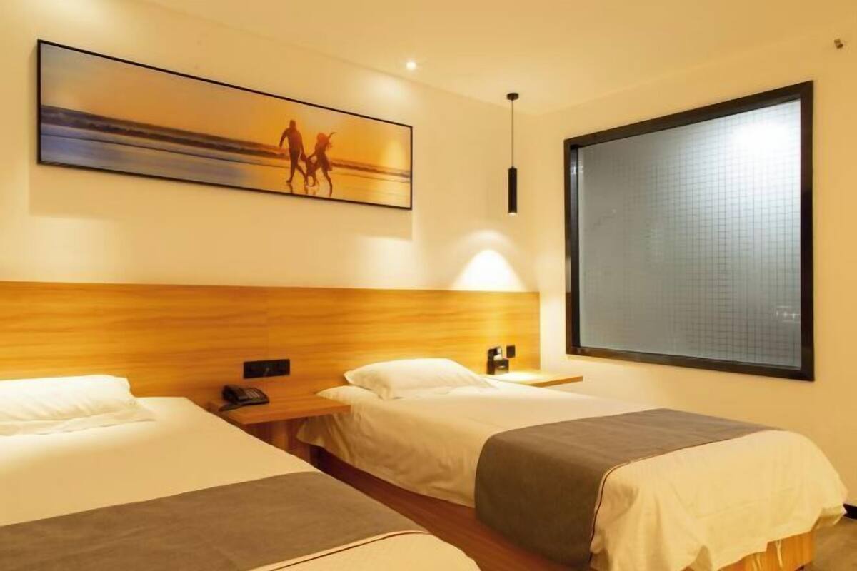 A hotel room with two beds, a large window, a painting on the wall, and a wooden headboard.