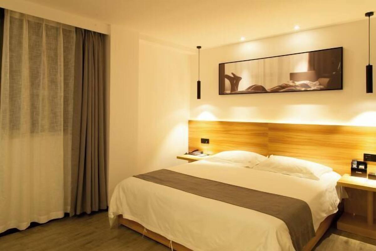 A hotel room with a bed, a nightstand, a wall-mounted artwork, and a window with curtains.