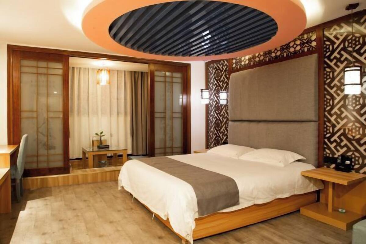 A hotel room with a bed, bedside table, lamp, and a view of a traditional sliding door.