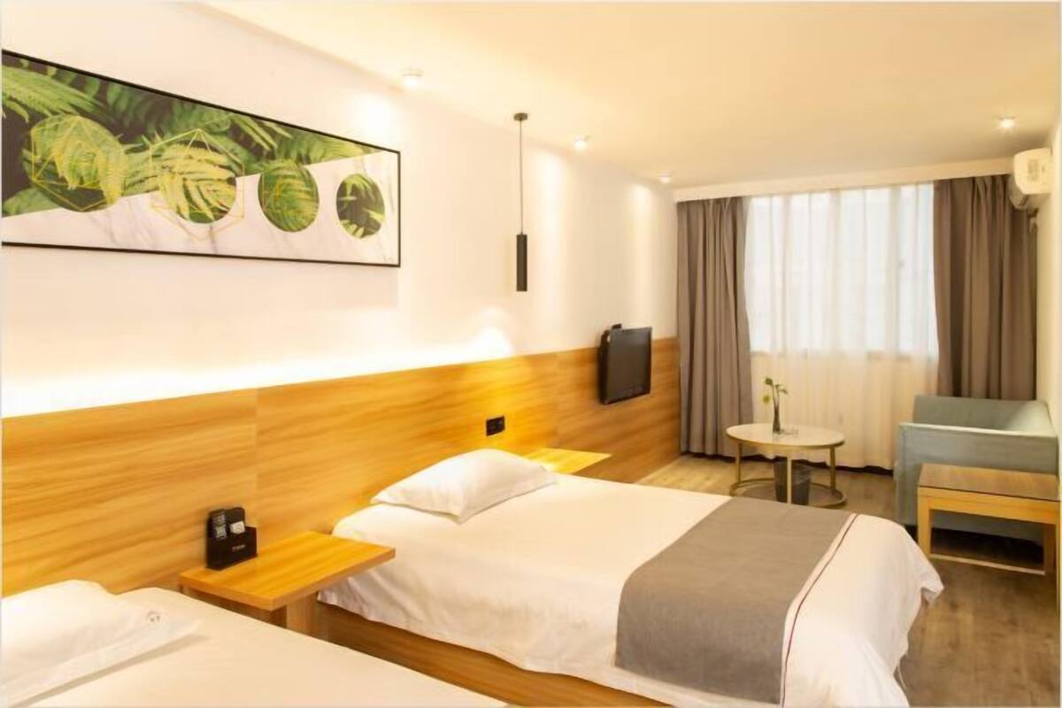A hotel room with two beds, a TV, a small table, and a window with curtains.