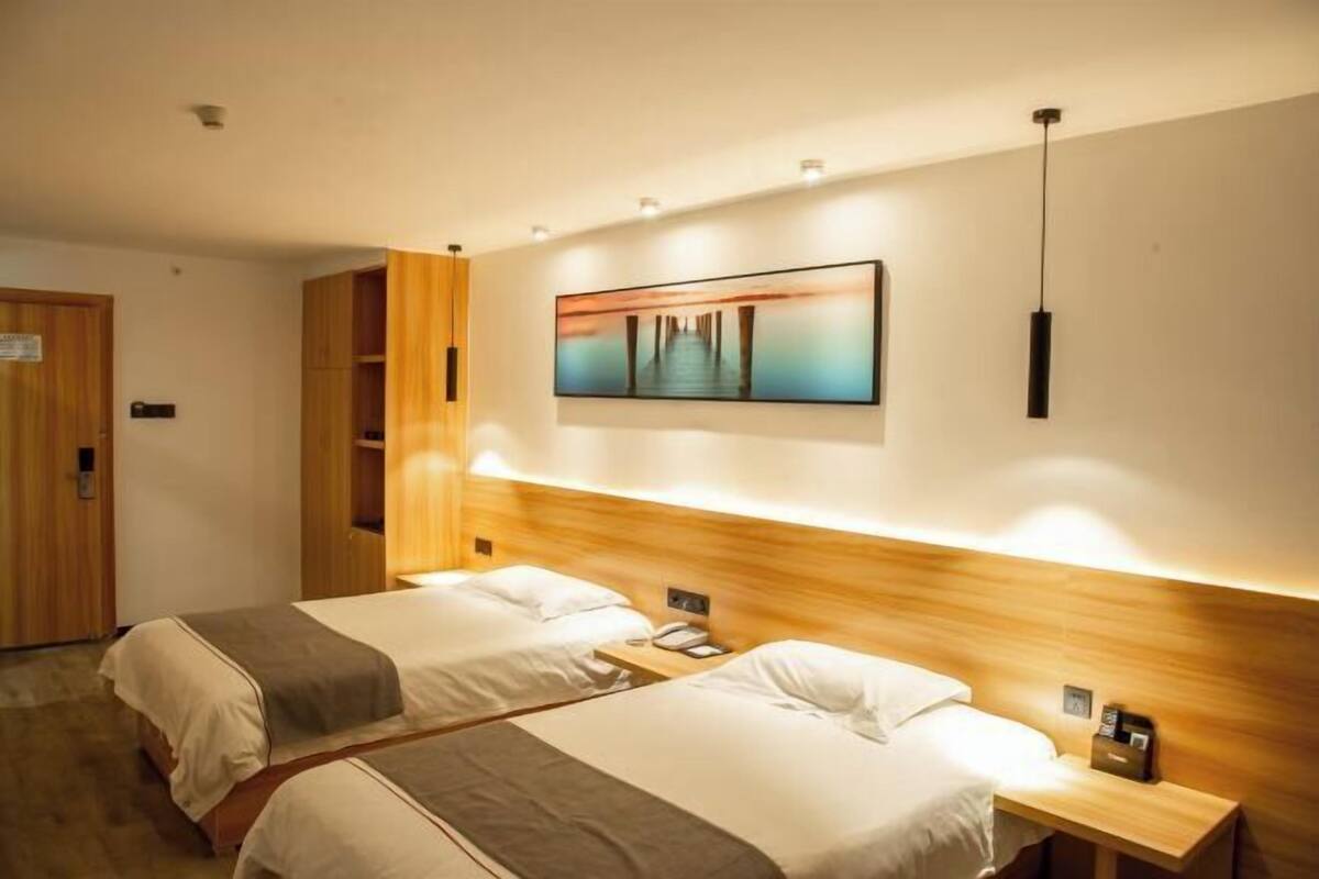 A hotel room with two beds, a wooden headboard, a wall-mounted painting, and a bedside table with a phone.