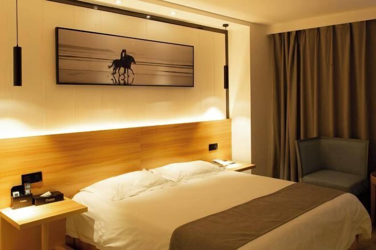 A hotel room with a large bed, a bedside table with a phone and a lamp, a chair, and a painting on the wall.