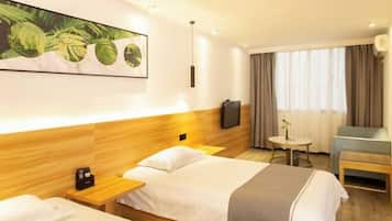 A hotel room with two beds, a TV, a small table, and a window with curtains.