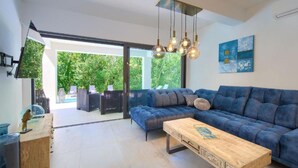 A modern living room with a blue sofa, wooden coffee table, and a view of a garden through large glass doors. - Wellness Villa (Vinodol)