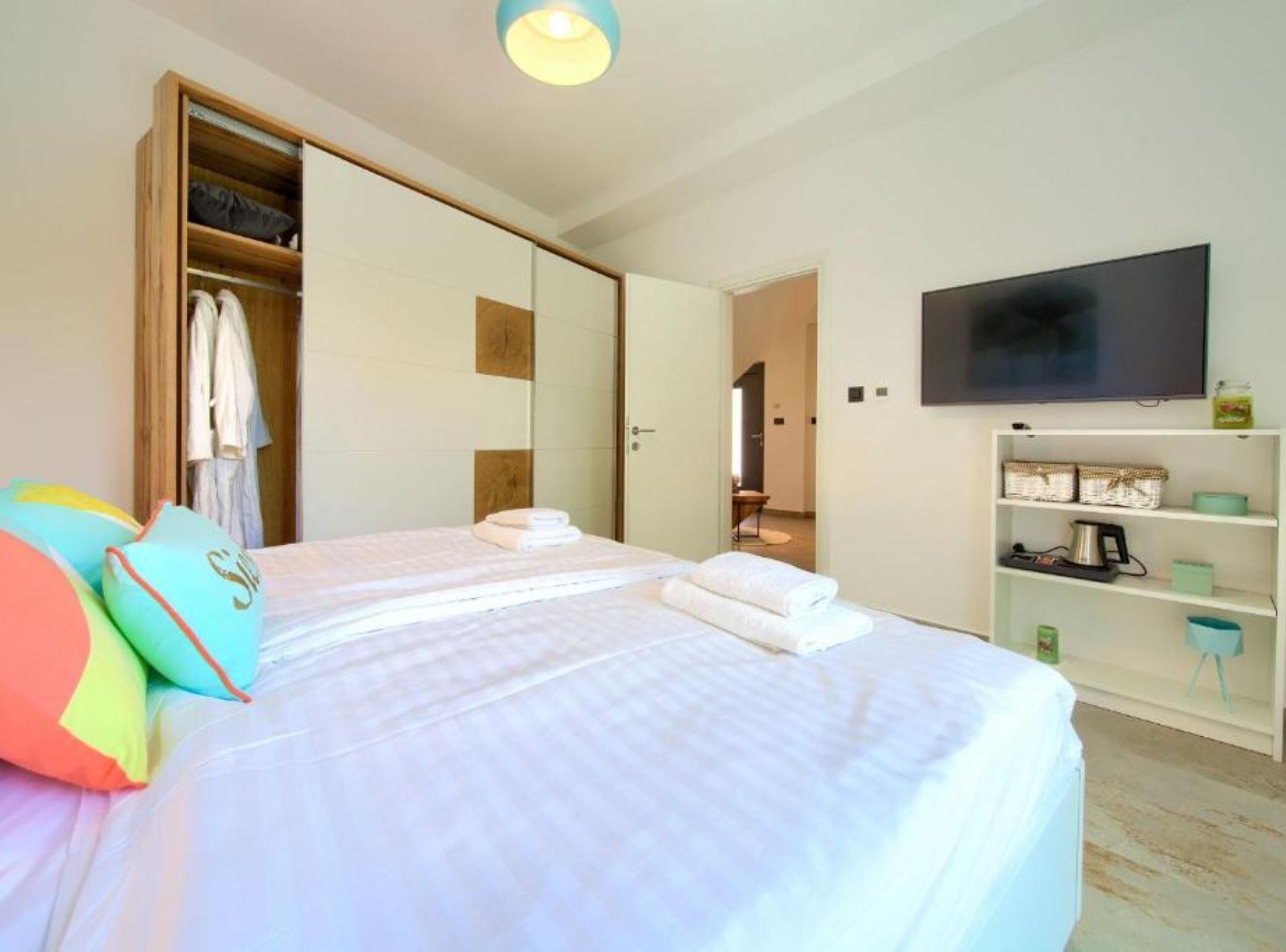 A bedroom with two beds, a wardrobe, a television, and a shelf with various items.
