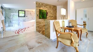A modern bathroom with a large bathtub, a shower area, and a marble floor. There is a dining area with two chairs and a table, and a wall with a green plant. - Wellness Villa (Vinodol)
