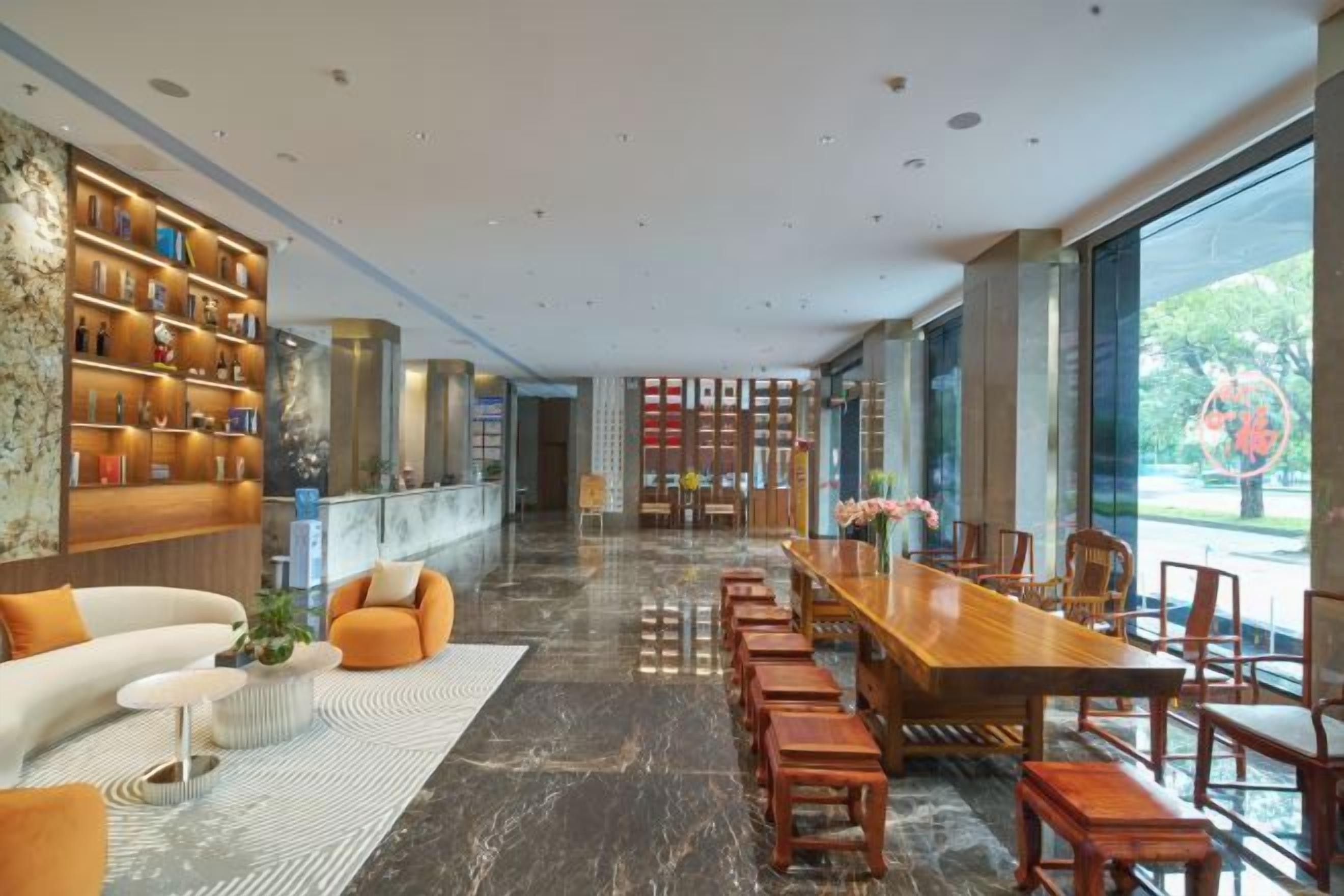 A spacious hotel lobby with a long dining table, comfortable seating, and a large bookshelf.