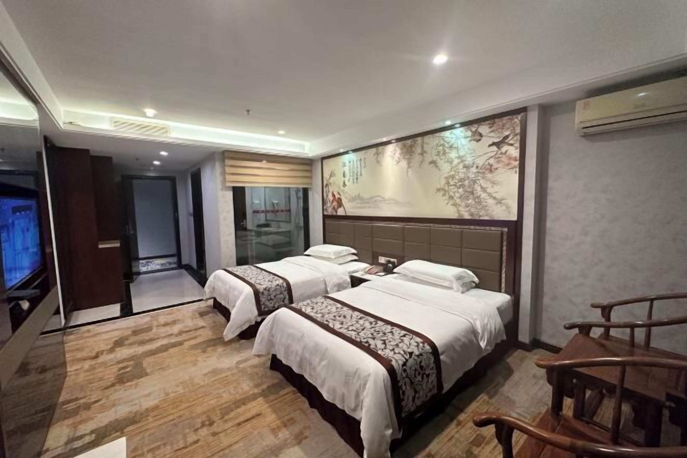 A hotel room with two beds, a TV, a wooden chair, and a large mural on the wall.