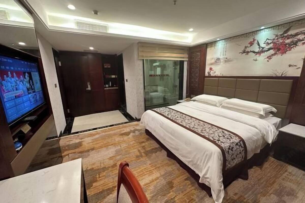 Ein Hotelzimmer mit einem großen Bett, einem Fernseher, einem Kleiderschrank und einem Badezimmer mit Glastür.