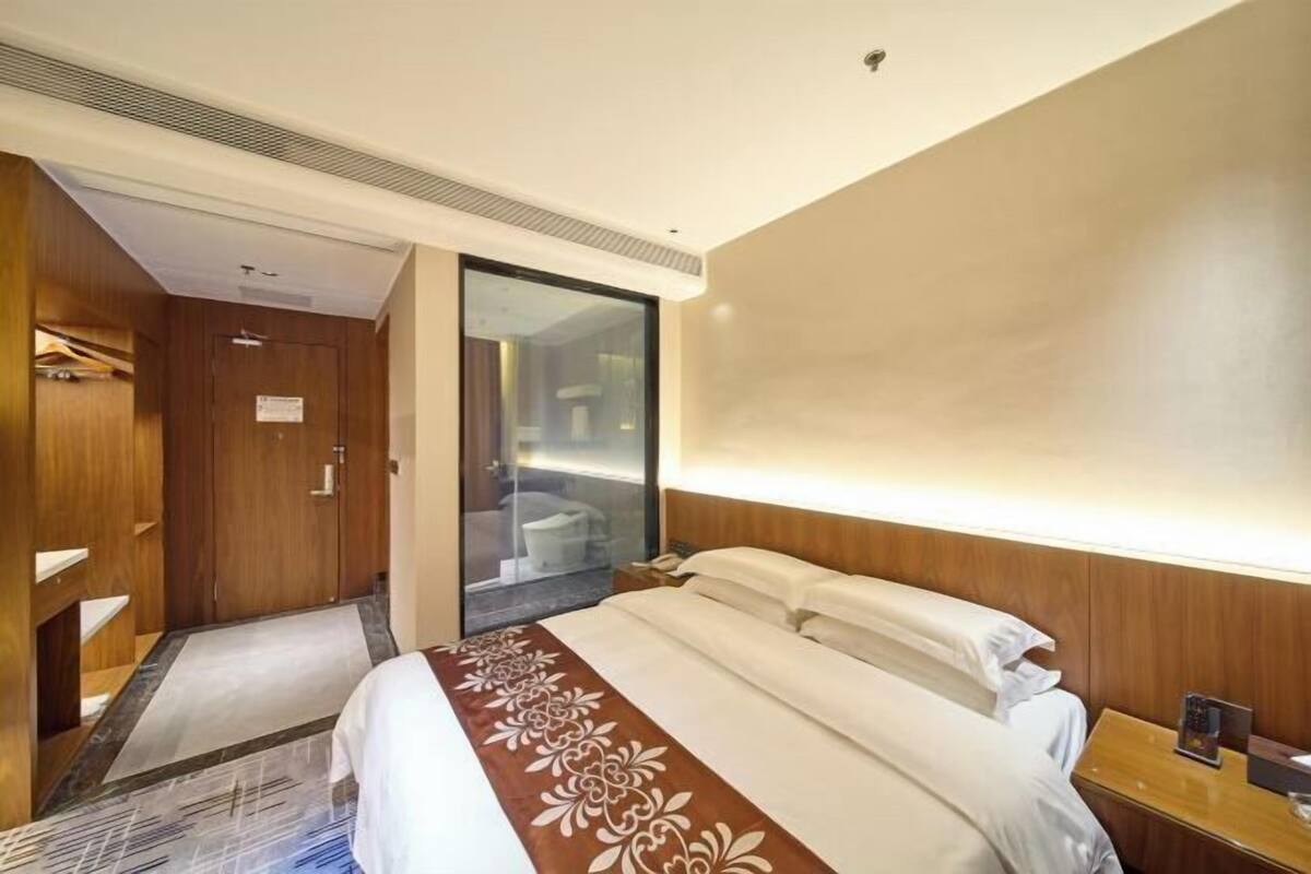 Ein Hotelzimmer mit einem Bett, einem Holzschrank, einem Badezimmer mit Glastür und einem Nachttisch mit Telefon.