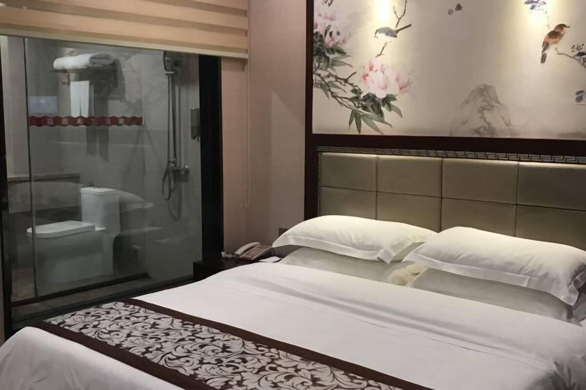 Ein Hotelzimmer mit einer gläsernen Duschkabine, einem Bett mit weißen Leinentüchern und einer Wand mit floralen und tierischen Motiven.