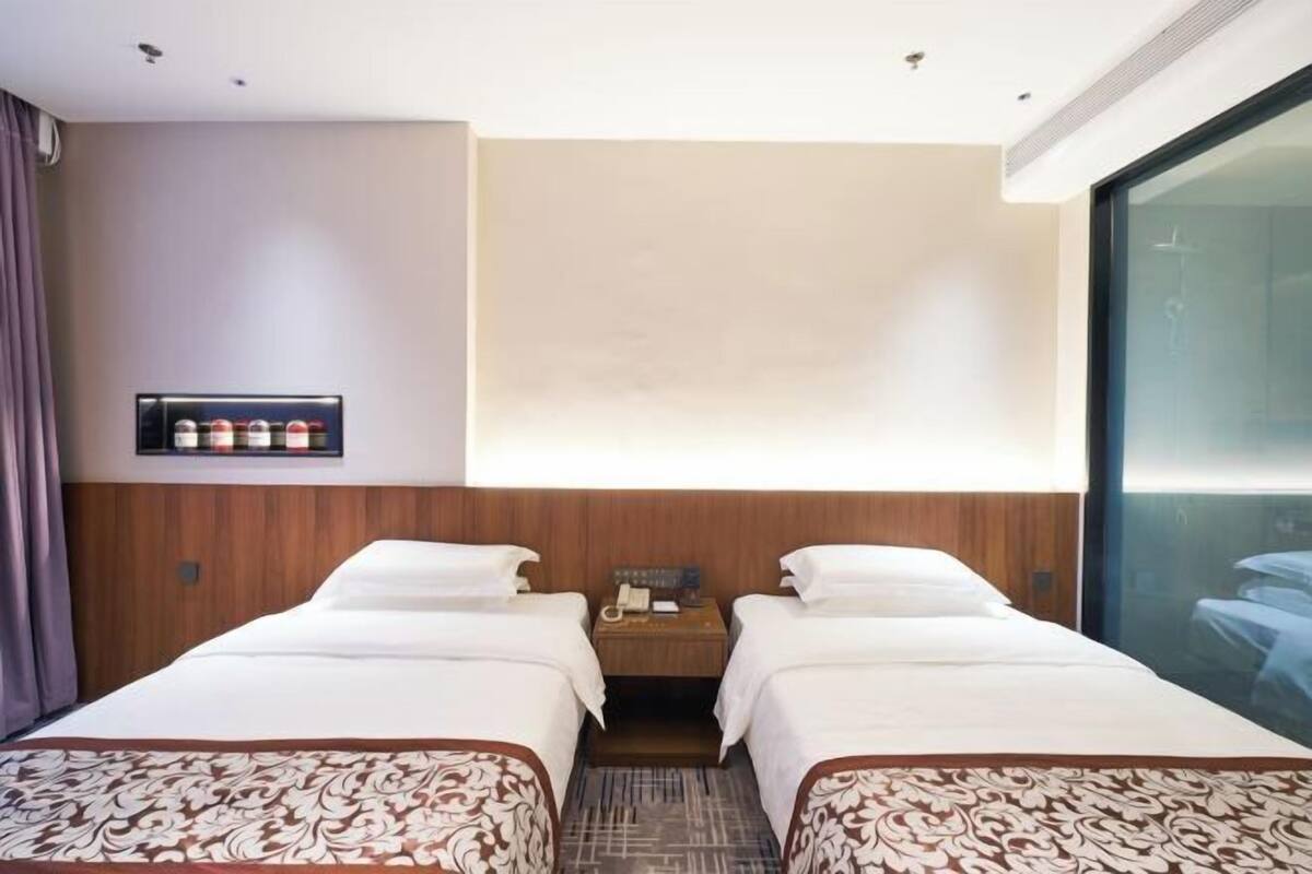 Ein Hotelzimmer mit zwei Betten, einem hölzernen Kopfteil, einem kleinen Nachttisch mit Telefon und einer Minibar.