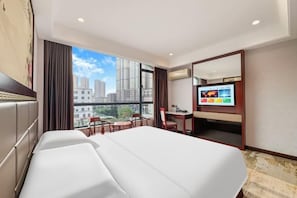A hotel room with a large bed, a desk, a chair, a TV, and a view of the cityscape. - Jiangmen Xinhui Chenpi Redwood Hotel (Xinhui Sports Center) (Jiangmen)