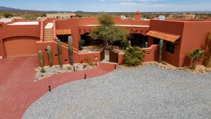 A desert-style building with a red facade, multiple cacti, and a gravel driveway. - Casa Richy - El Dorado Ranch Rental (San Felípe)
