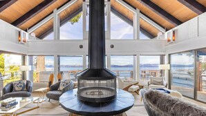 Un amplio salón con chimenea de piedra, asientos cómodos y grandes ventanales con vistas a las montañas y al lago.