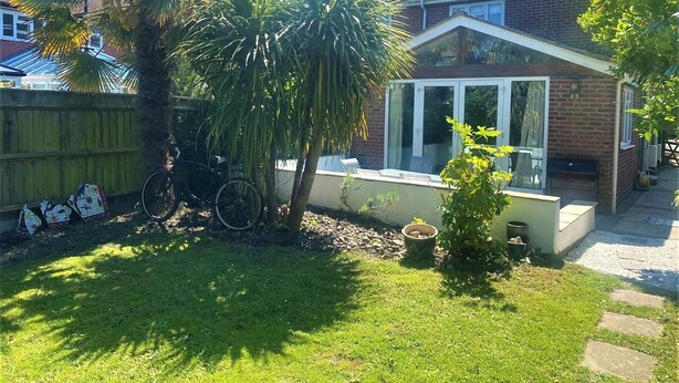 Une cour arrière d’une maison, avec une terrasse, un vélo et un petit jardin.