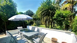 Une terrasse extérieure avec une table à plateau de verre, des chaises en métal et un grand parasol.