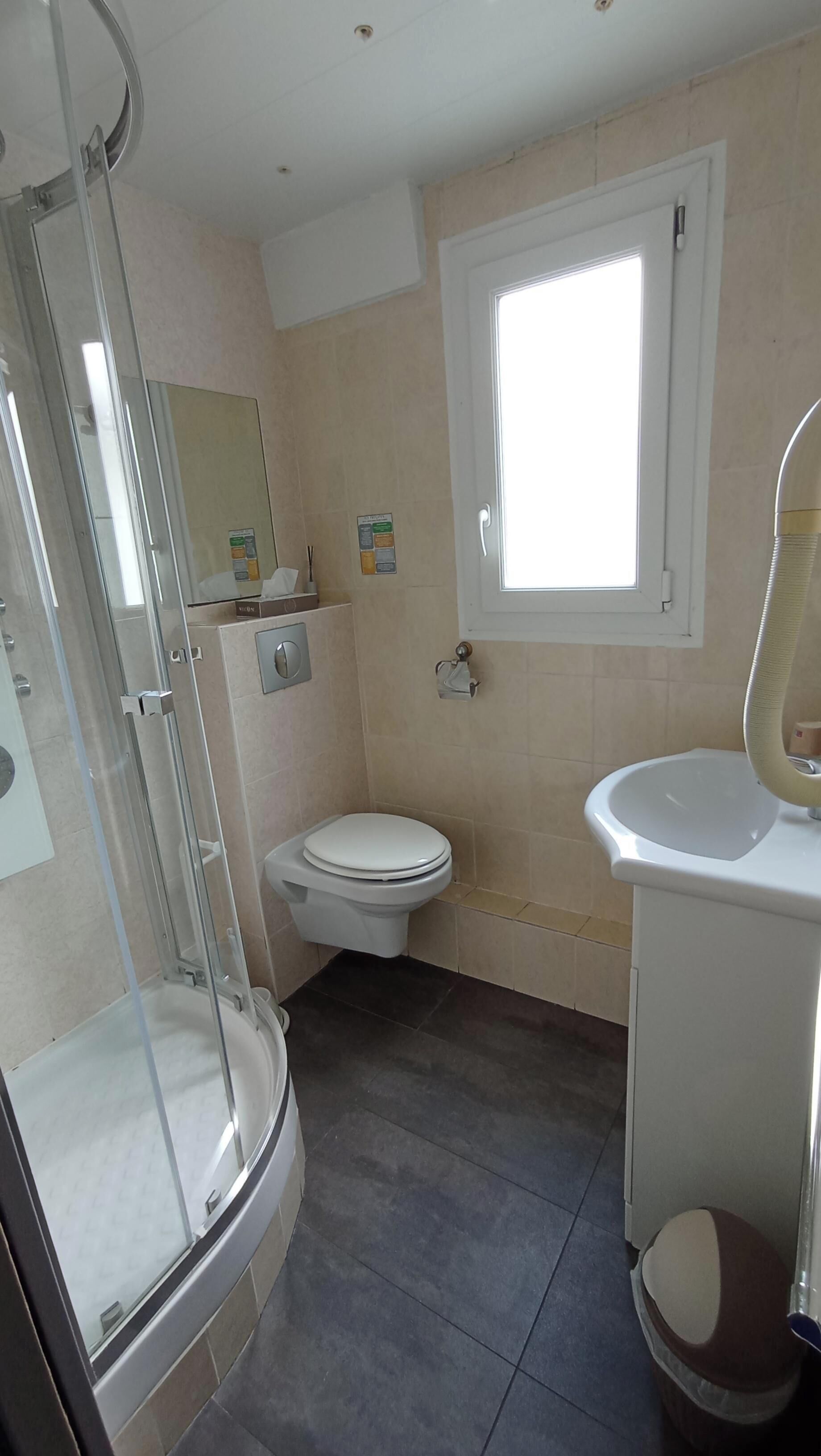 A bathroom with a glass shower enclosure, a toilet, a sink, and a window.