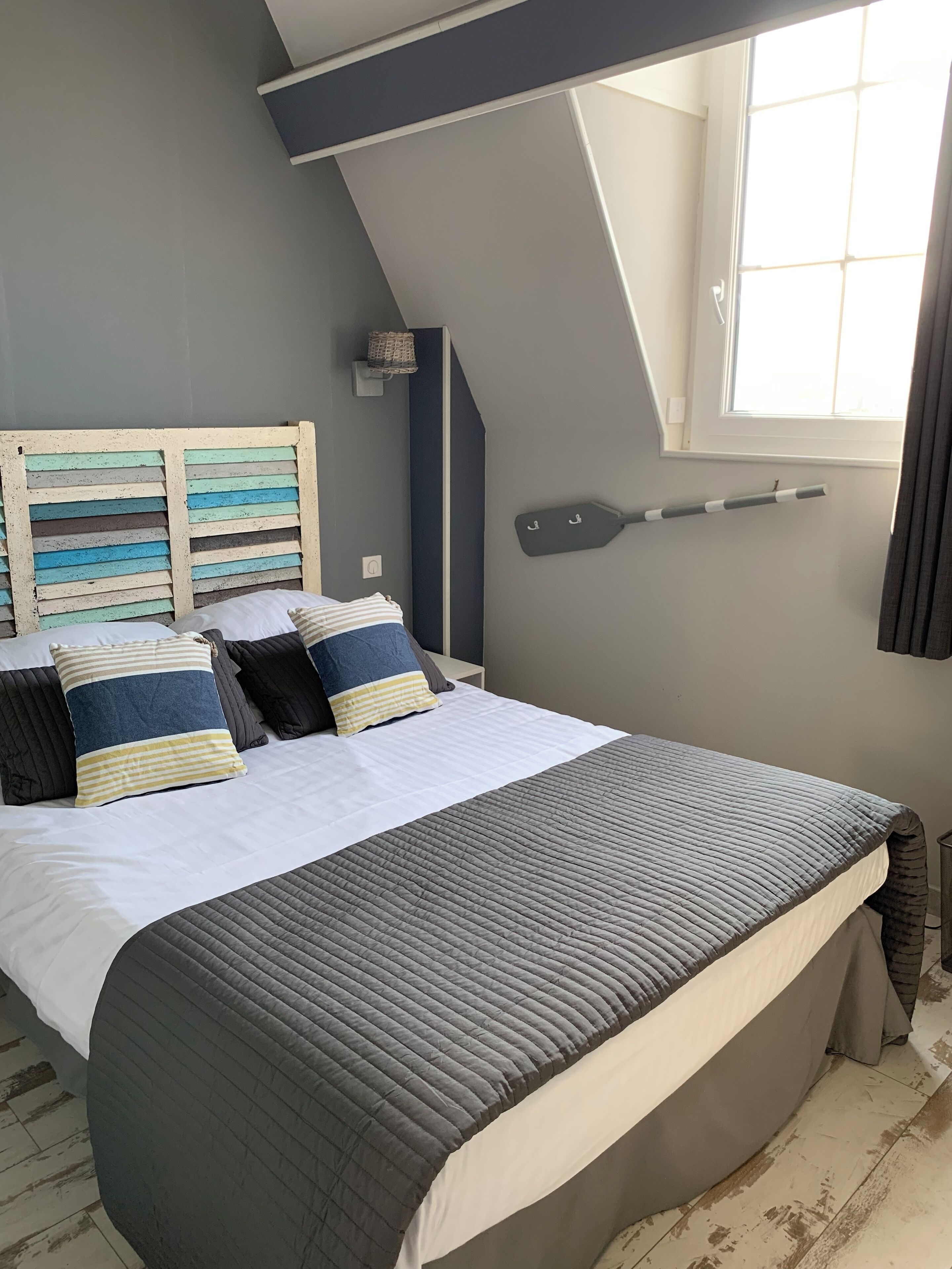 Un dormitorio con una cama grande, techo inclinado, ventana con cortinas y una tabla de surf de pared.