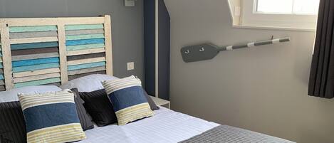 Un dormitorio con una cama grande, techo inclinado, ventana con cortinas y una tabla de surf de pared.