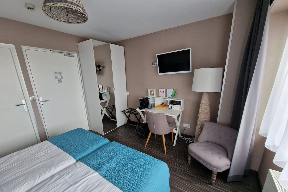 Une chambre d’hôtel avec deux lits, un bureau équipé d’un ordinateur, une chaise, une télévision et une lampe.