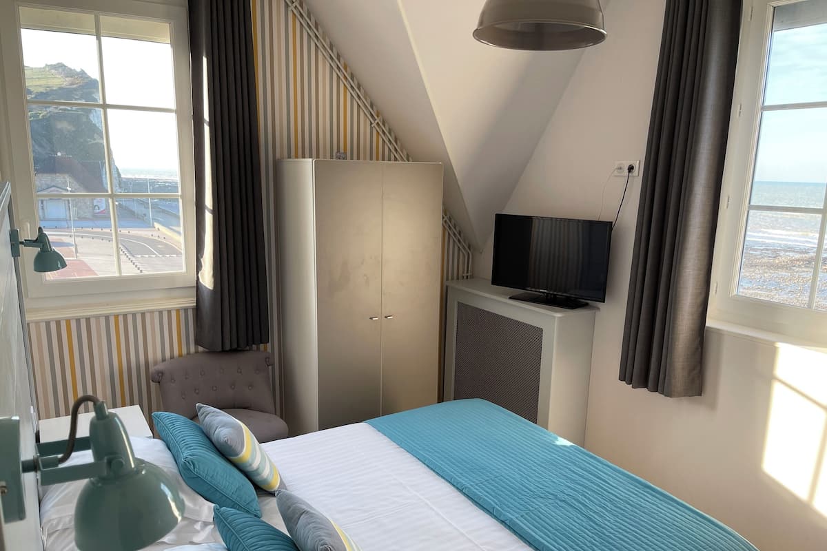 Une chambre à coucher comprenant un lit, une télévision, une armoire et une fenêtre donnant sur la mer.