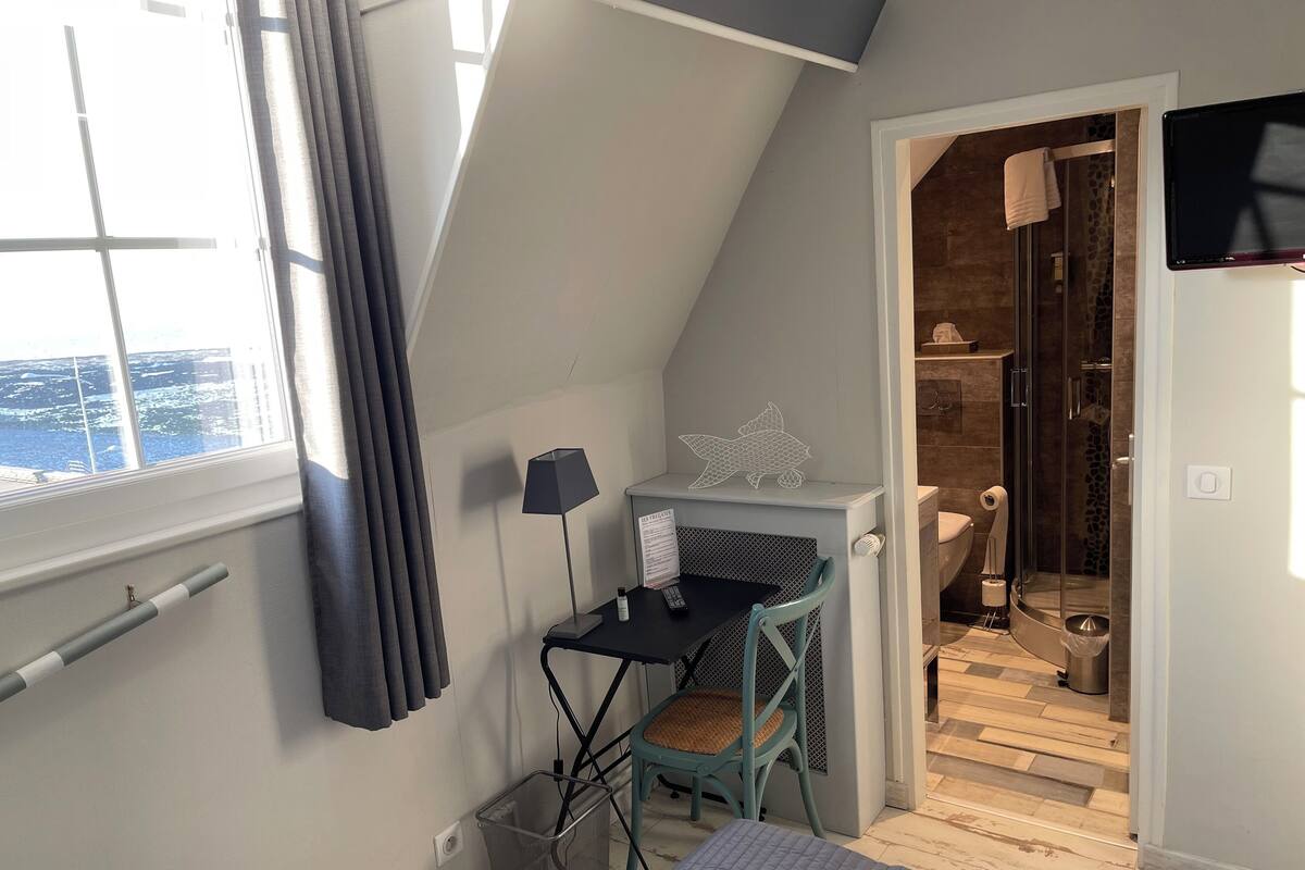 Une petite pièce moderne avec un plafond en pente, un bureau avec une chaise, un lit et un espace douche.