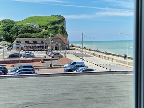 A coastal road with parked cars, a café, and a view of the sea.