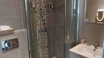 Et moderne badeværelse med en glasafskærmet brusekabine, toilet og håndvask med spejl.