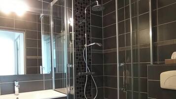 Een moderne badkamer met een douchecabine van glas, donkere betegelde muren, een wastafel met spiegel en een toilet.